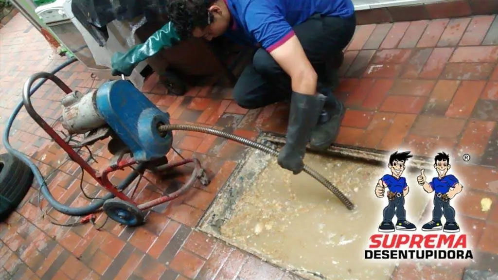Técnico desentupindo caixa de gordura com máquina rotativa em piso externo
